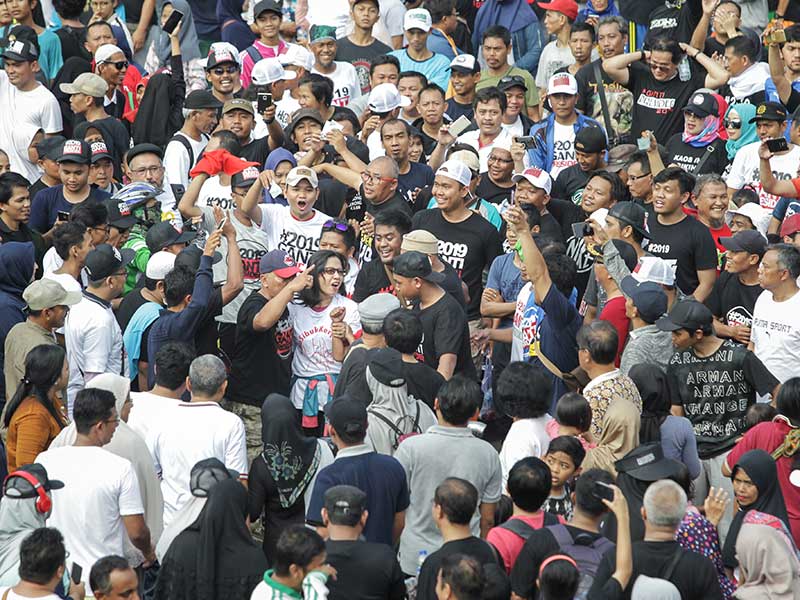 Seorang perempuan dengan kaus bertuliskan ‘#DiaSibukKerja’ yang terpisah dari rombongan dikerumuni massa pengguna kaus bertuliskan ‘#2019GantiPresiden’ saat melintas di Bundaran Hotel Indonesia, Jakarta, Minggu (29/4/2018)