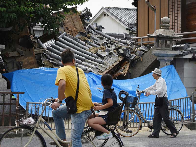 Warga melintas di depan sebuah rumah yang hencur akibat gempa yang mengguncang wilayah Osaka,  Jepang