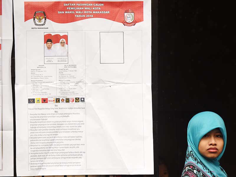  Warga melintas di dekat daftar pasangan Calon Walikota-Wakil Walikota Makassar saat pemungutan suara pemilihan Walikota-Wakil Walikota Makassar di TPS 01 Keluarahan Tidung Mariolo Makassar, Sulawesi Selatan, Rabu (27/6/2018)