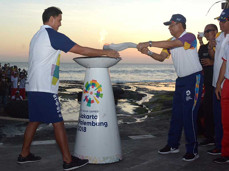 ktor Hamish Daud (kiri) menyerahkan obor kepada Sekda Kabupaten Tabanan, Nyoman Wirna Ariwangsa (keempat kanan) saat menyambut Torch Relay Asian Games 2018 di objek wisata Tanah Lot, Kabupaten Tabanan, Bali, Senin (23/7/2018). 