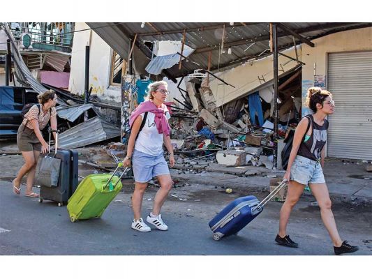 TINGGALKAN KAWASAN WISATA: Wisatawan asing melintas di depan rumah yang roboh akibat gempa di Kecamatan Pemenang, Tanjung, Lombok Utara, Nusa Tenggara Barat, kemarin. Para wisatawan yang berkunjung ke Gili Trawangan, Gili Air, dan Gili Meno pascagempa bers
