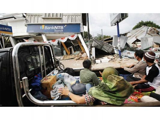 LOMBOK UTARA LUMPUH: Warga dengan menaiki mobil bak terbuka melintas di antara bangunan yang roboh akibat gempa di pusat perekonomian kawasan Pemenang, Lombok Utara, Nusa Tenggara Barat, kemarin. Pascagempa bekekuatan 7 pada skala Richter yang diikuti gemp