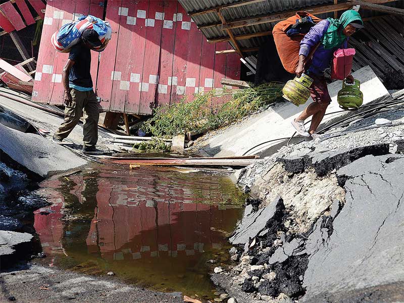 MENGUMPULKAN BARANG YANG BISA DIGUNAKAN: Warga membawa barang-barang yang masih bisa digunakan di antara reruntuhan rumah dan jalan yang hancur di kawasan Petobo, Sulawesi Tengah, kemarin. Petobo merupakan salah satu wilayah terdampak gempa yang paling par