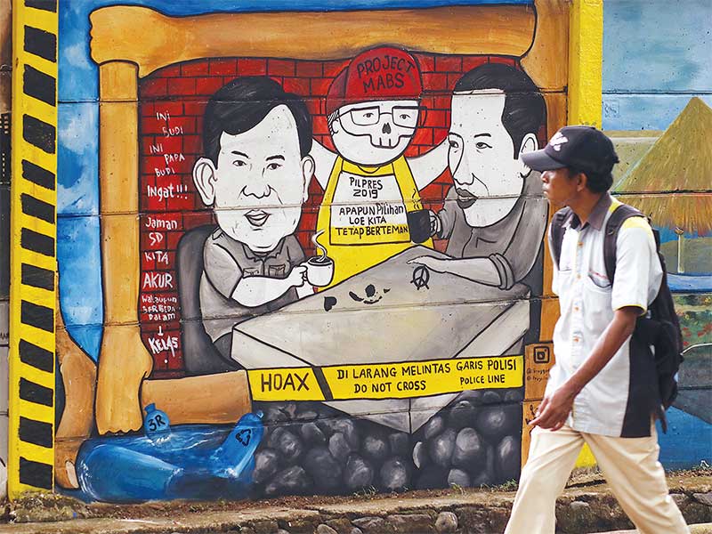 MURAL PILPRES: Warga melintas di dekat gambar mural capres Joko Widodo dan Prabowo Subianto di Jalan Juanda, Depok, Jawa Barat, kemarin. Gambar mural tersebut memiliki pesan agar masyarakat tetap damai dan berteman meski berbeda pilihan calon presiden di P
