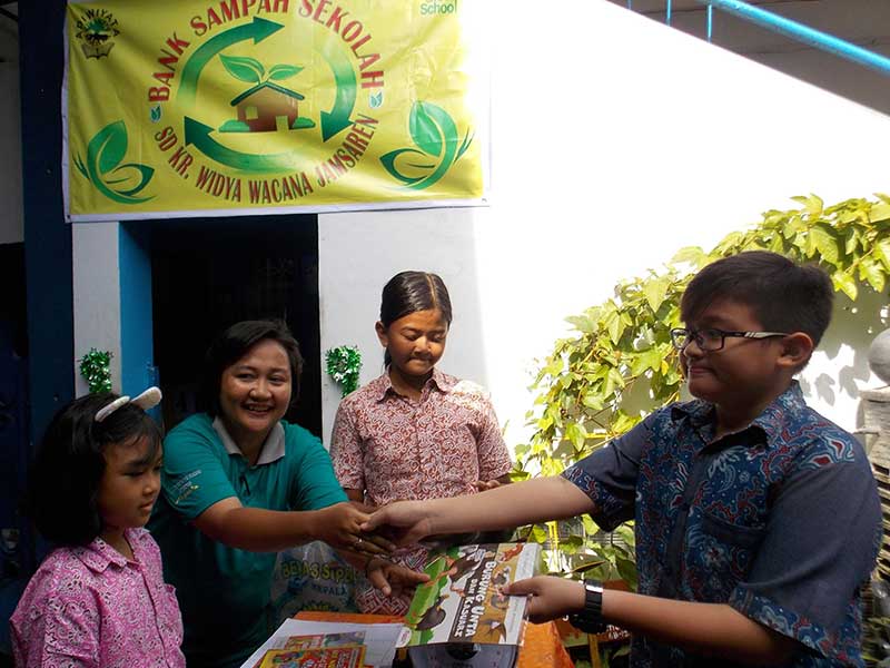 Kepala Sekolah SD Kr. Widya Wacana Jamsaren, Kota Surakarta, Jawa Tengah, Six Hastuti Ariasati menyerahkan buku bacaan kepada siswa yang menyetorkan sampah di bank sampah sekolah tersebut, Sabtu (26/1/2019).