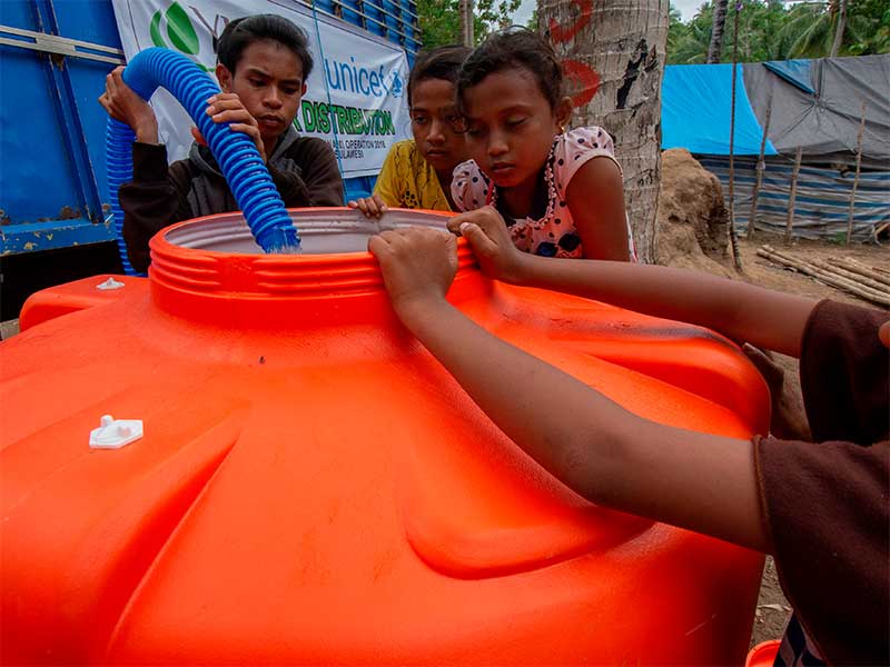 Sejumlah anak menyaksikan pengisian tandon dengan air bersih di kamp pengungsi Desa Toaya Vunta, Donggala, Sulawesi Tengah, Jumat (21/12/2018). 