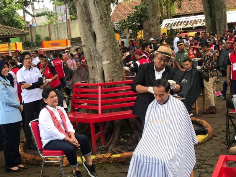 Kang Herman tukang cukur asal Garut sedang mencukur rambut Presiden Joko Widodo dalam acara cukur massal yang digelar di lokasi wisata Situ Bagendit, Garut, Sabtu (19/1/2019). Herman mengaku grogi tapi bangga berkesempatan mencukur rambut Presiden.