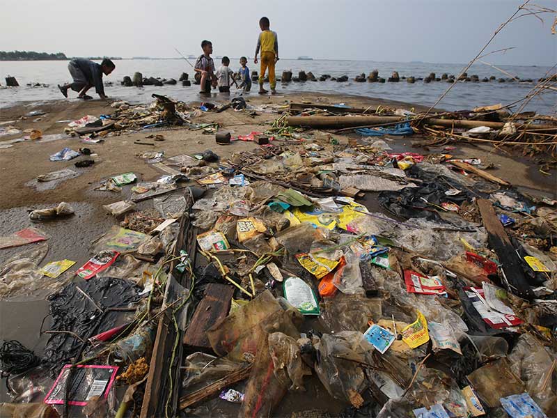 Anak-anak bermain di tanggul pemecah ombak yang dipenuhi sampah plastik karena terbawa angin Barat Laut di Pelabuhan Kali Adem, Jakarta Utara, Selasa (8/1/2019).