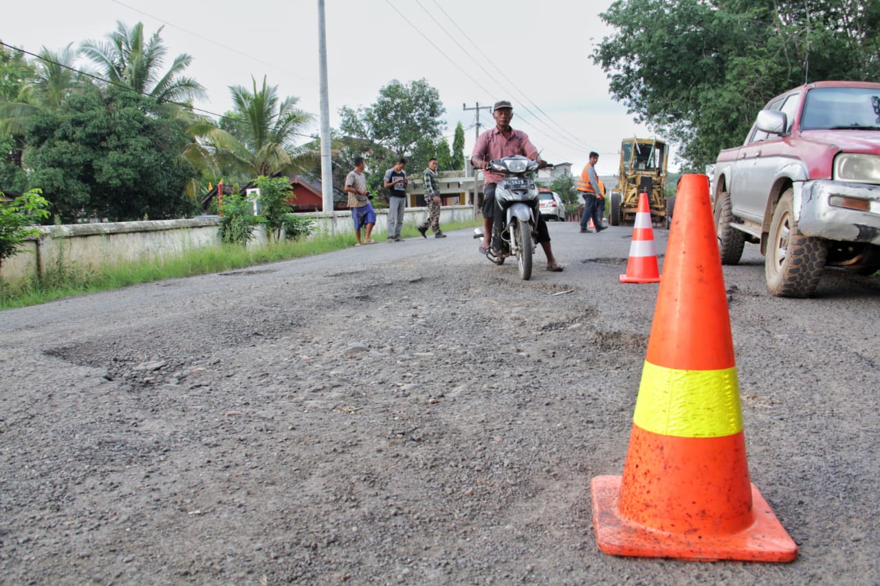 Para pengendara melalui kondisi jalan yang rusak.