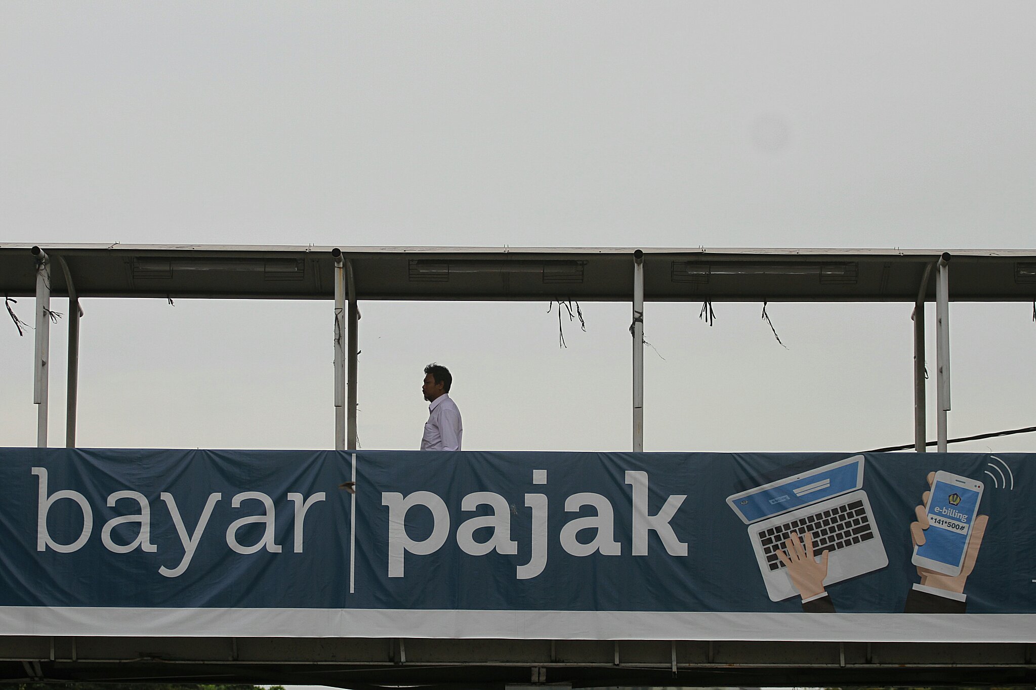 Pejalan kaki melintasi papan sosialisasi pembayaran pajak secara online di Jakarta pada 2016.