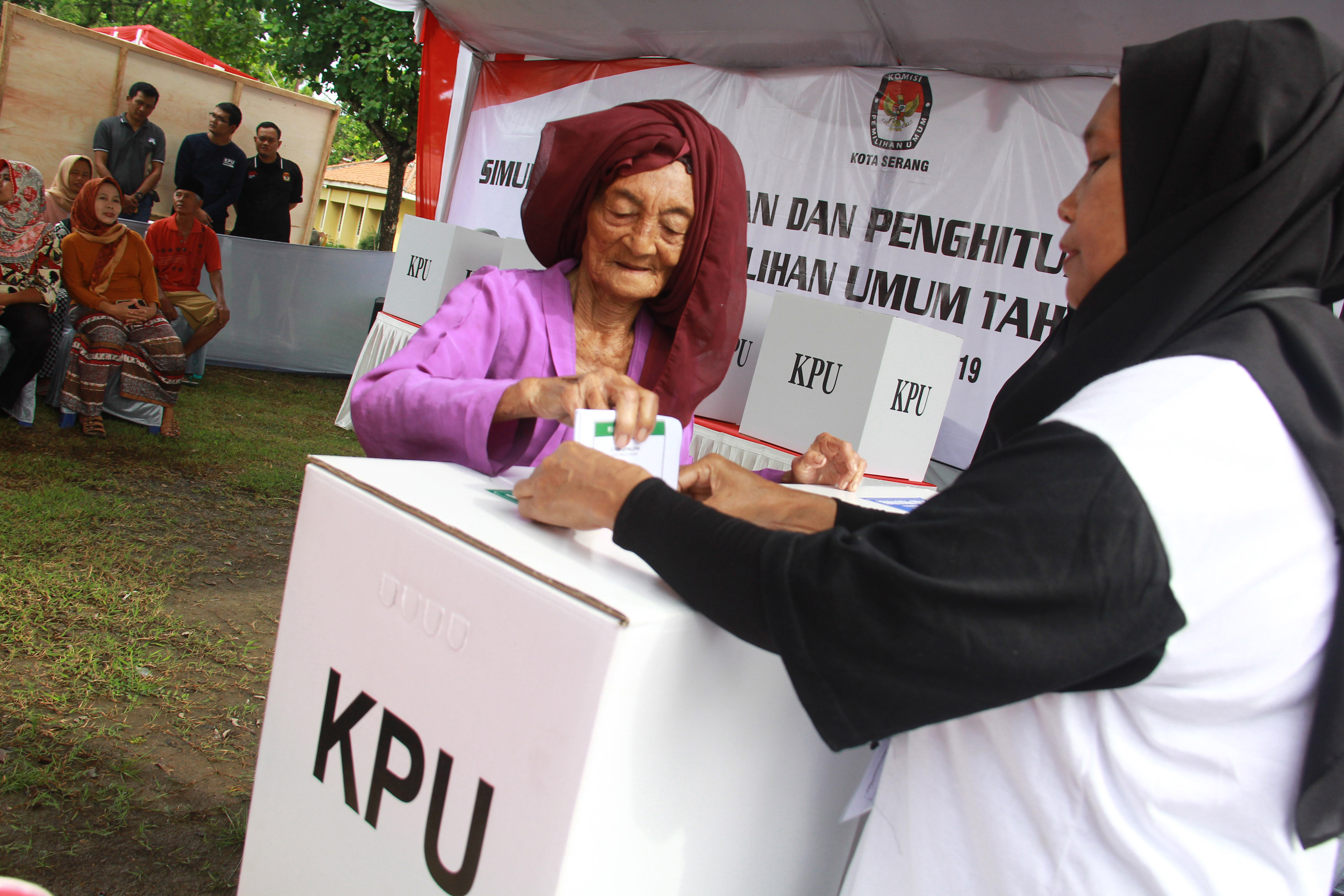 Petugas TPS membantu warga lanjut usia memasukan surat suara ke dalam kotak suara saat simulasi Pemilu di TPS Cinanggung, Kota Serang, Banten (24/3/2019).