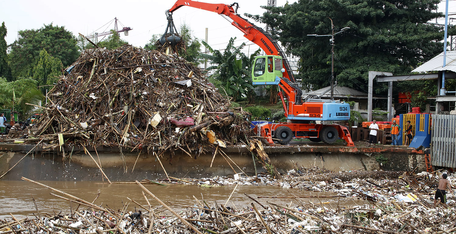 Petugas kebersihan menggunakan alat berat mengeruk dan membersihkan sampah yang menumpuk di Pintu Air Manggarai, Jakarta.