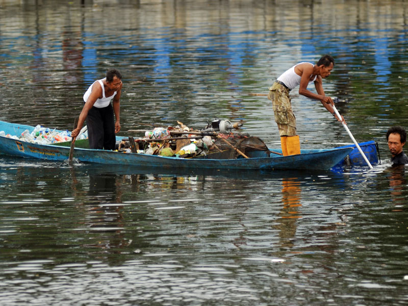 Petugas Dinas Lingkungan Hidup mengumpulkan sampah yang mengapung menggunakan perahu.