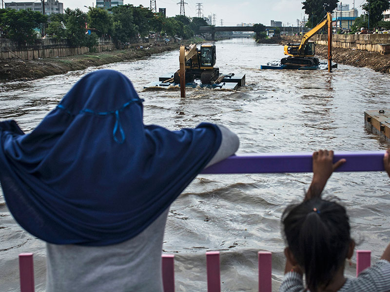 KONSEP NATURALISASI SUNGAI DI IBU KOTA: Warga menyaksikan alat berat mengeruk endapan lumpur sungai Ciliwung, di Kanal Banjir Barat (KBB).