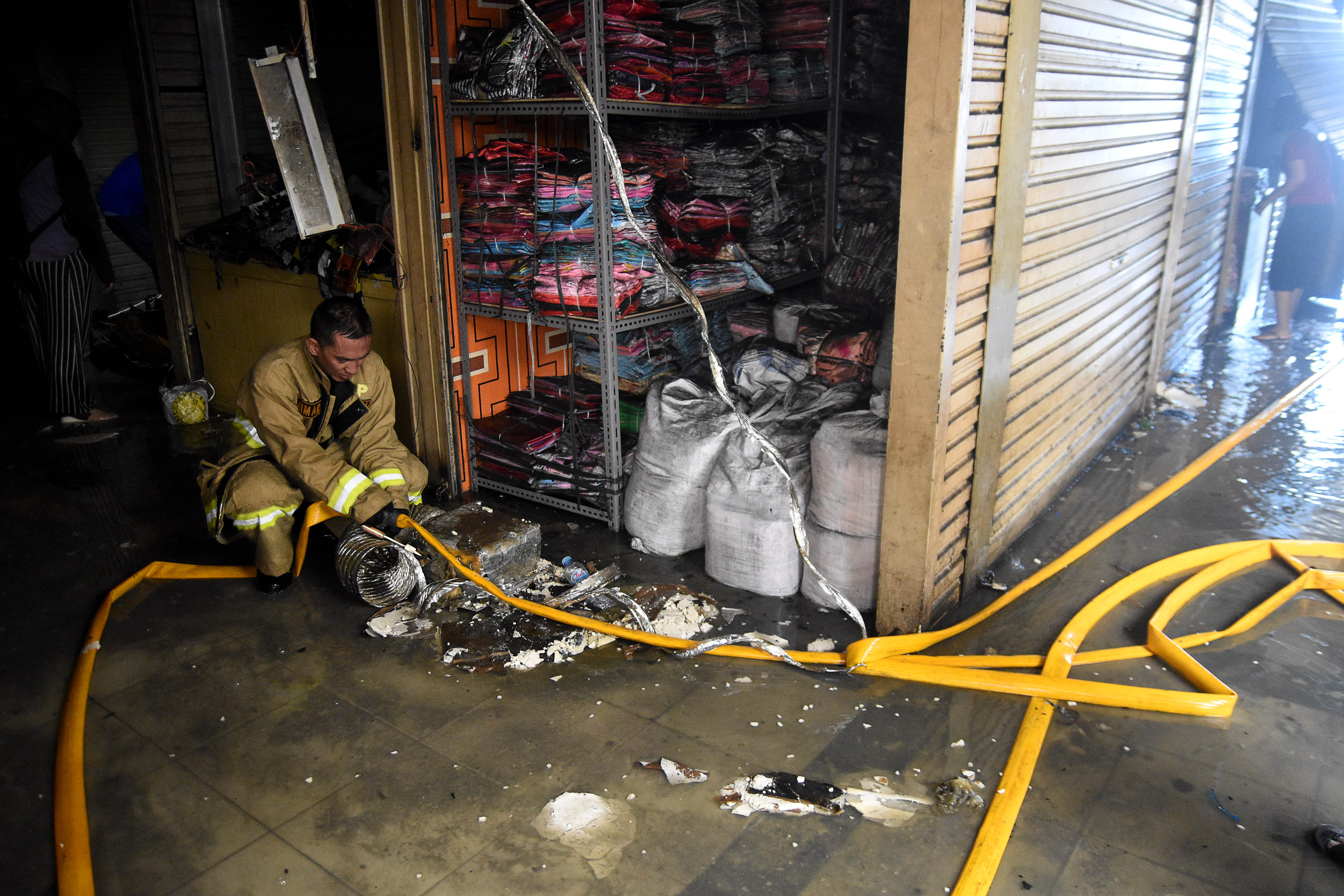 Petugas pemadam kebakaran menggulung selang pemadam usai melakukan pembasahan pada kebakaran yang terjadi di Gudang baju blok C Pasar Tanah 