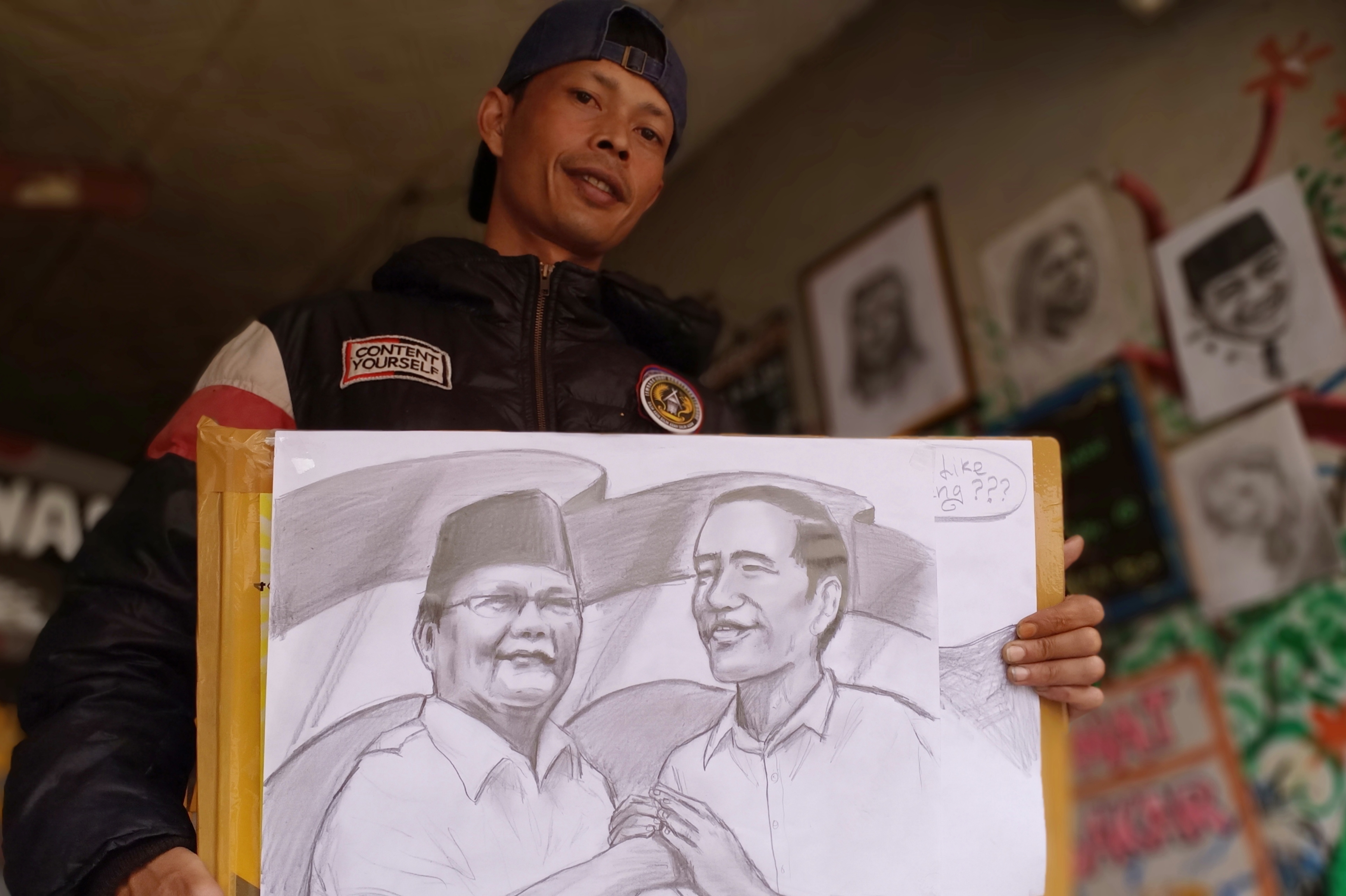 Aep Wahyudin menunjukan lukisan sketsa wajah dua calon presiden