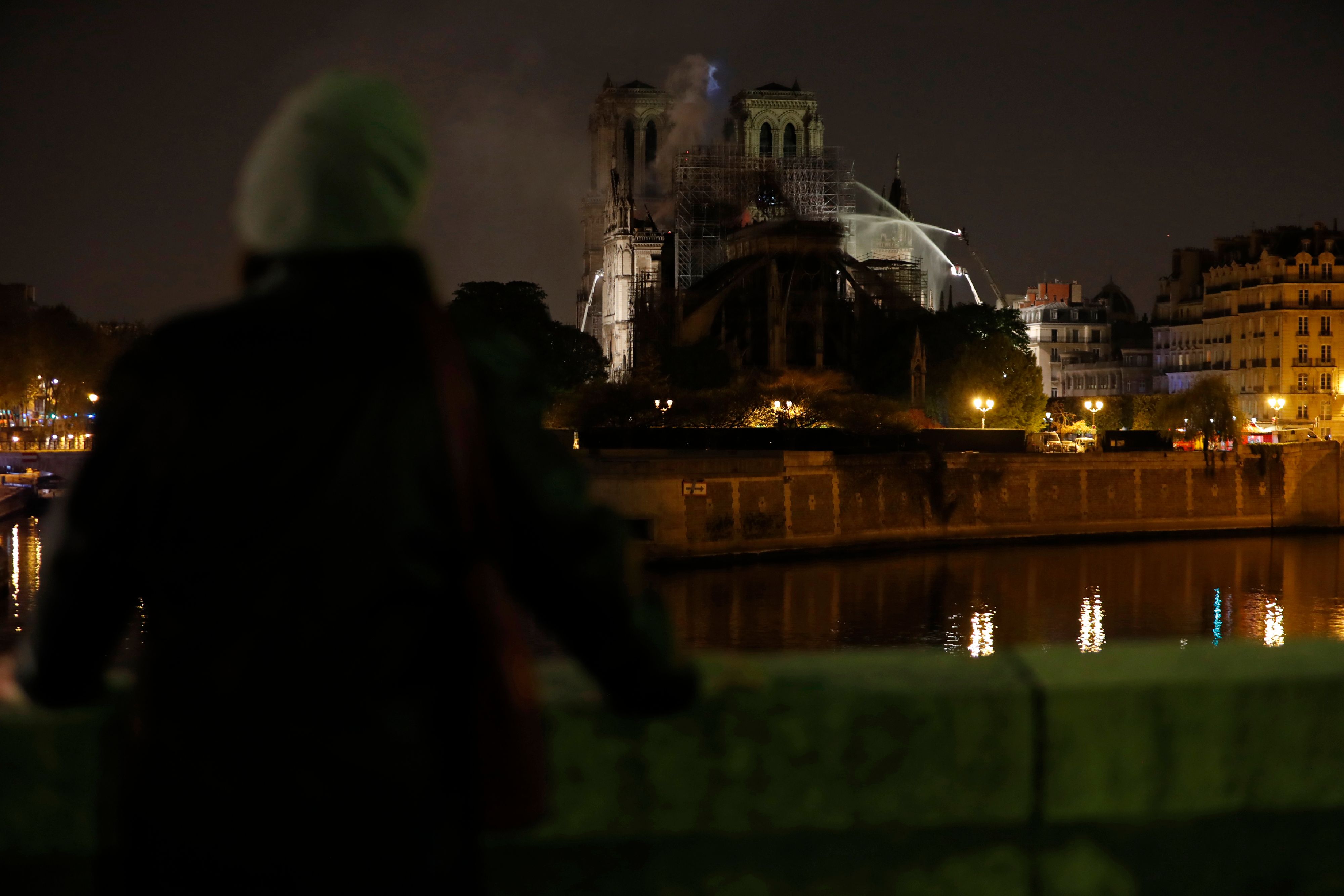 Warga Paris menyaksikan pasukan pemadam kebakaran berusaha memadamkan api yang melanda Katedral Notre Dame.