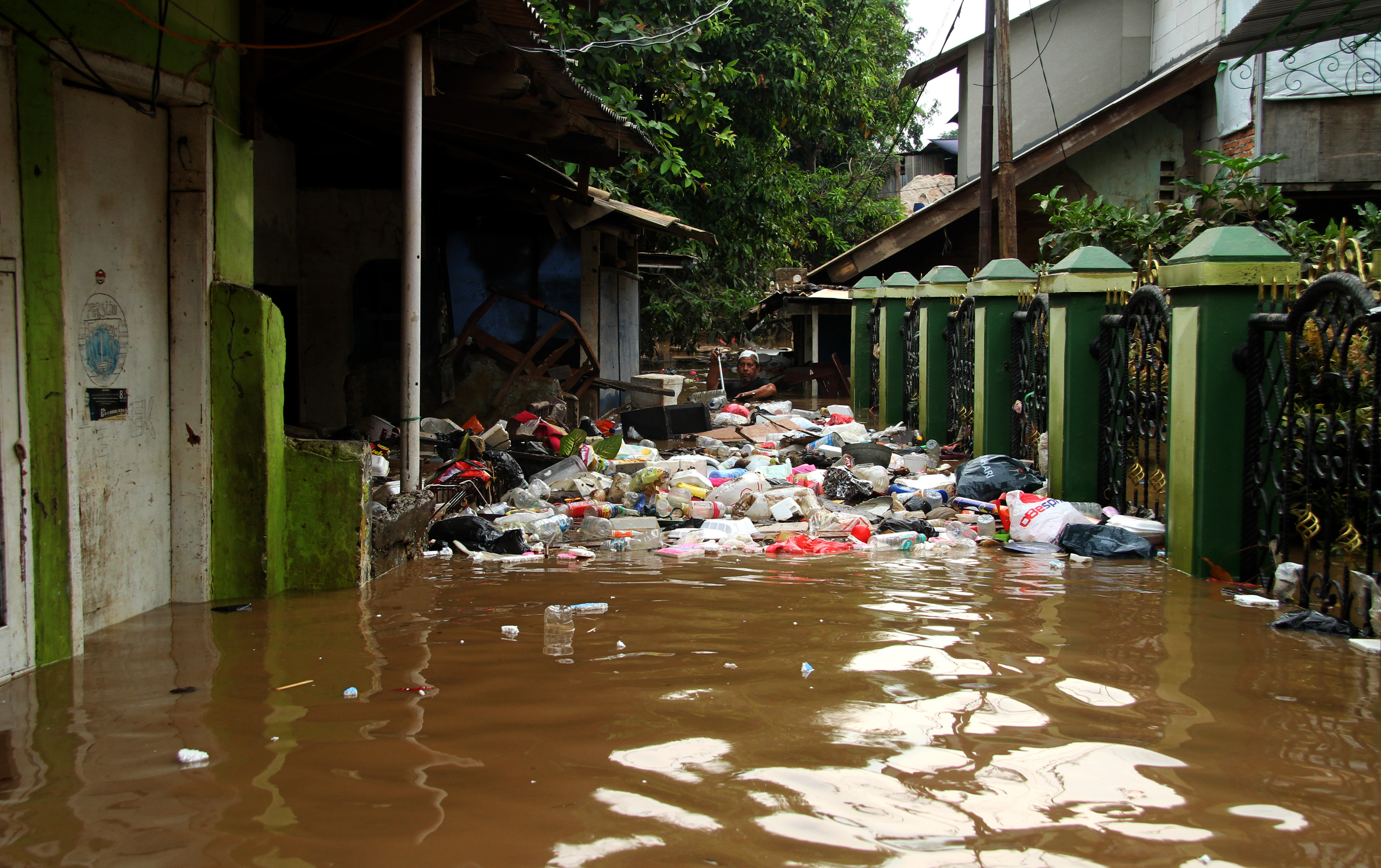 Seorang warga berusaha membersihkan sampah yang terbawa aliran banjir di kawasan permukiman penduduk Cililitan Kecil, Jakarta.
