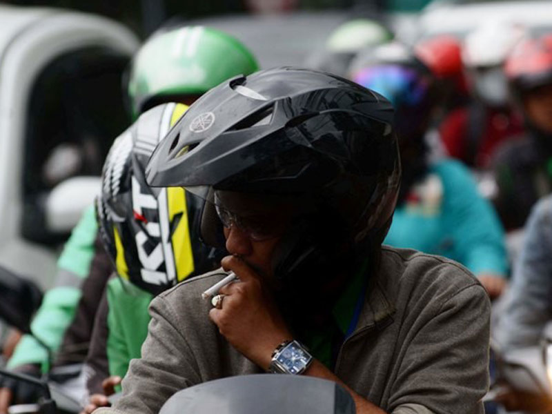 Pengendara sepeda motor menikmati rokok saat berkendaraan di Jalan Raya.