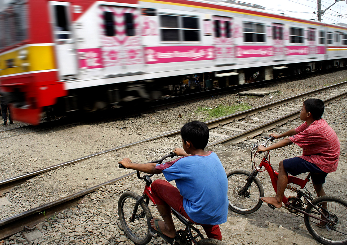  Anak-anak menghentikan laju sepeda mereka saat menunggu kereta melintas di pelintasan liar kereta api tanpa palang pintu 