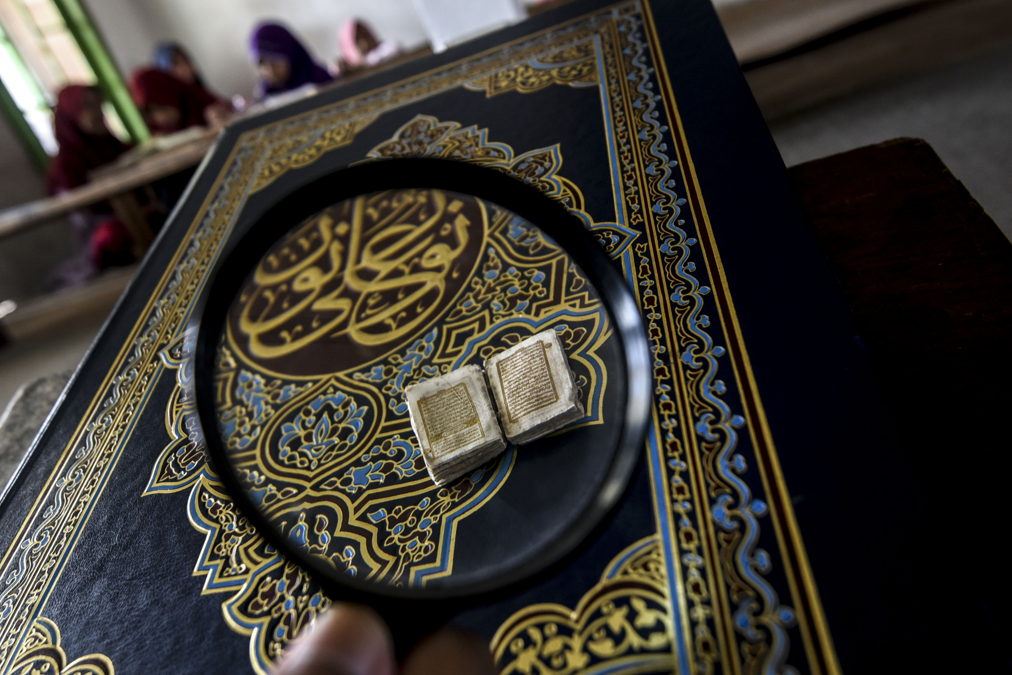  Sebuah Alquran terkecil di dunia dengan latar belakang santri yang sedang mengaji
