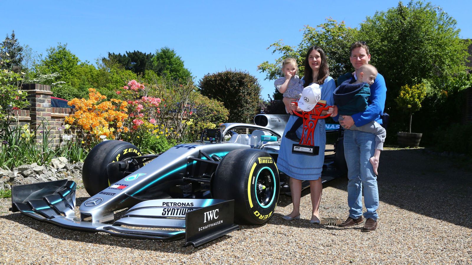 Harry Shaw bersama keluarganya berpose di dekat mobil Lewis Hamilton di kediaman mereka.
