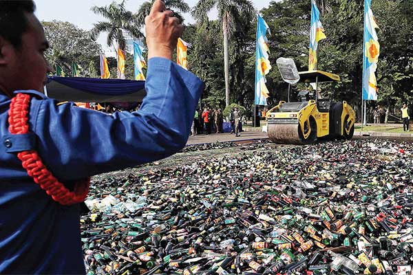 Petugas menggunakan alat berat memusnahkan ribuan botol minuman keras ilegal di Lapangan Monas, Jakarta Pusat, kemarin.