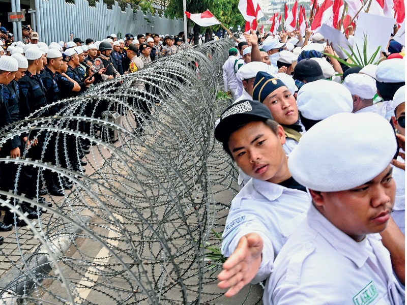 Petugas kepolisian dengan berkalung serban dan berkopiah putih menjaga pengunjuk rasa saat melakukan demonstrasi menentang dugaan kecurangan