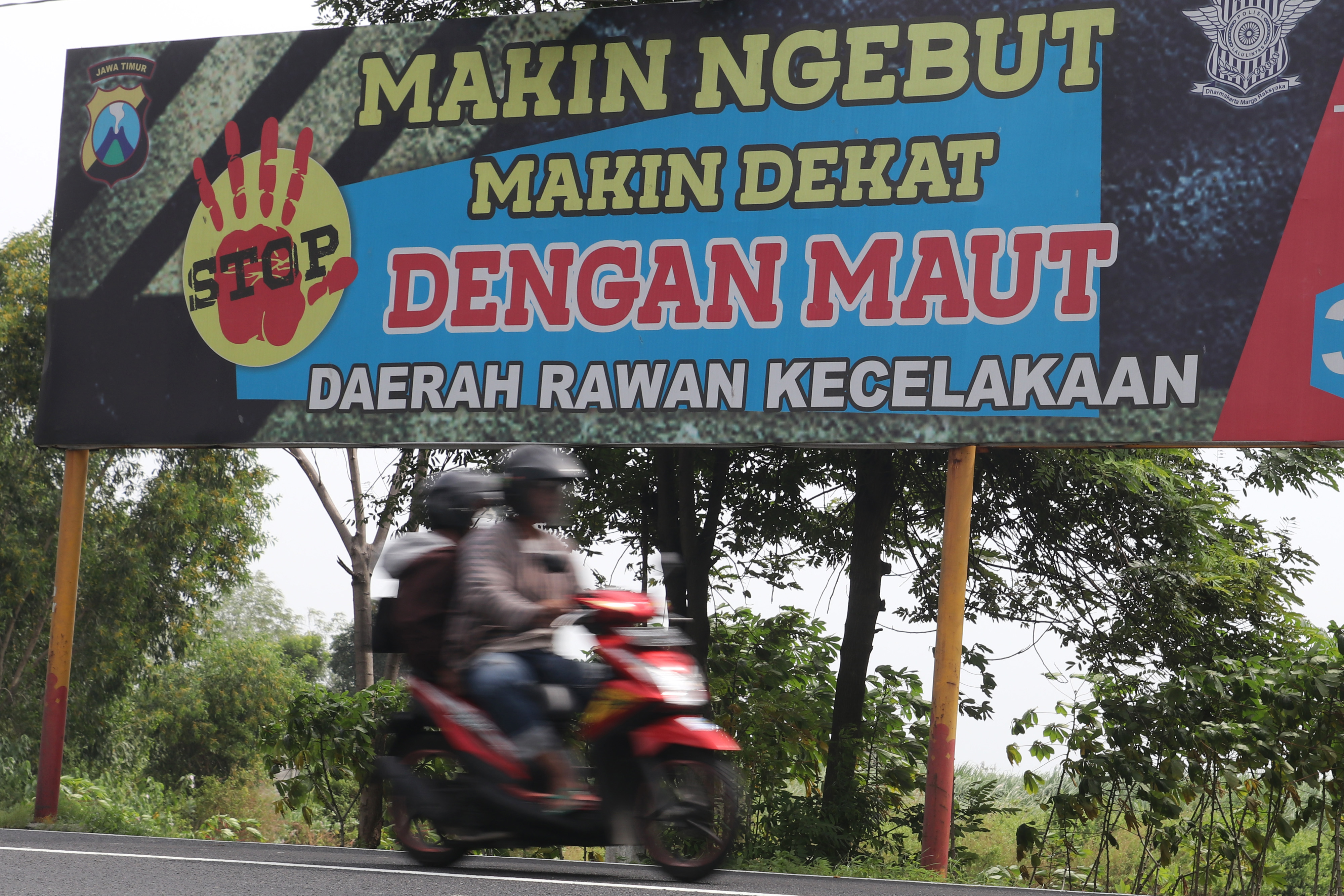  Pengendara sepeda motor melintas di dekat spanduk peringatan berhati-hati berkendara di Jalan Raya Kertosono-Madiun, di Nganjuk