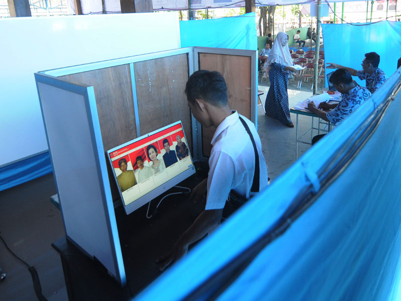 Pemilih mengamati foto calon kepala desa pada layar komputer saat melakukan pemilihan kepala desa (Pilkades) sistem 