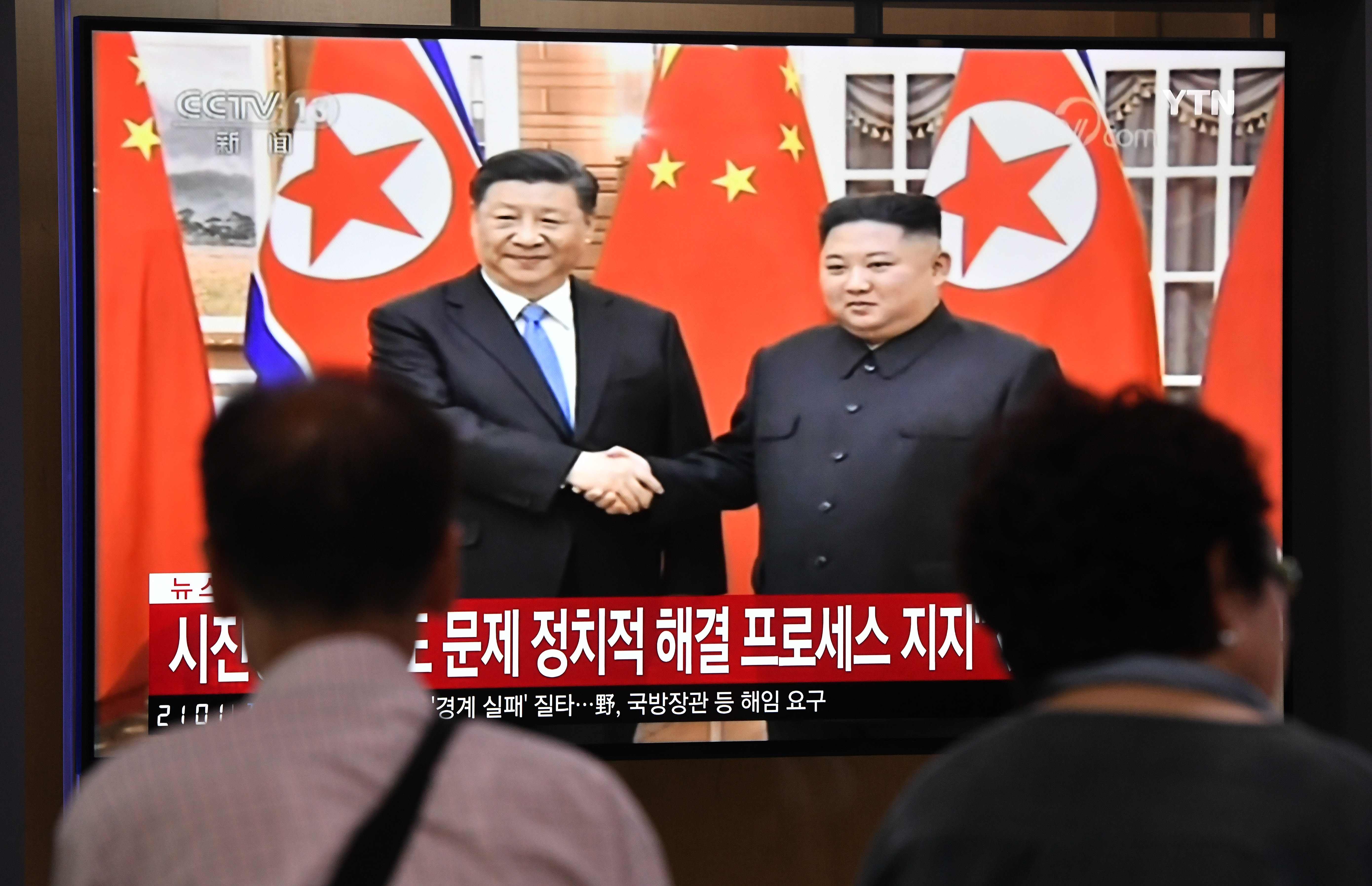 berita televisi yang memperlihatkan pemimpin Korea Utara Kim Jong Un berjabat tangan dengan Presiden Cina Xi Jinping