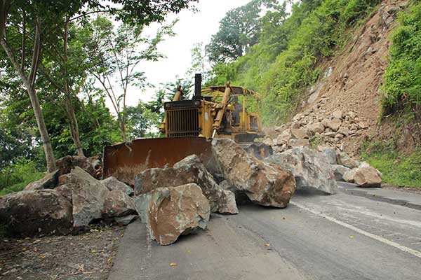 Sebuah kendaraan alat berat digunakan untuk menyingkirkan longsoran berupa batu cadas di jalur selatan Lumajang