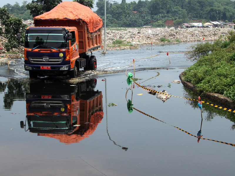 Pengendara truk pengangkut sampah melintasi jalan yang digenangi air limbah, di kawasan di Tempat Pembuangan Akhir (TPA) Sumur Batu.