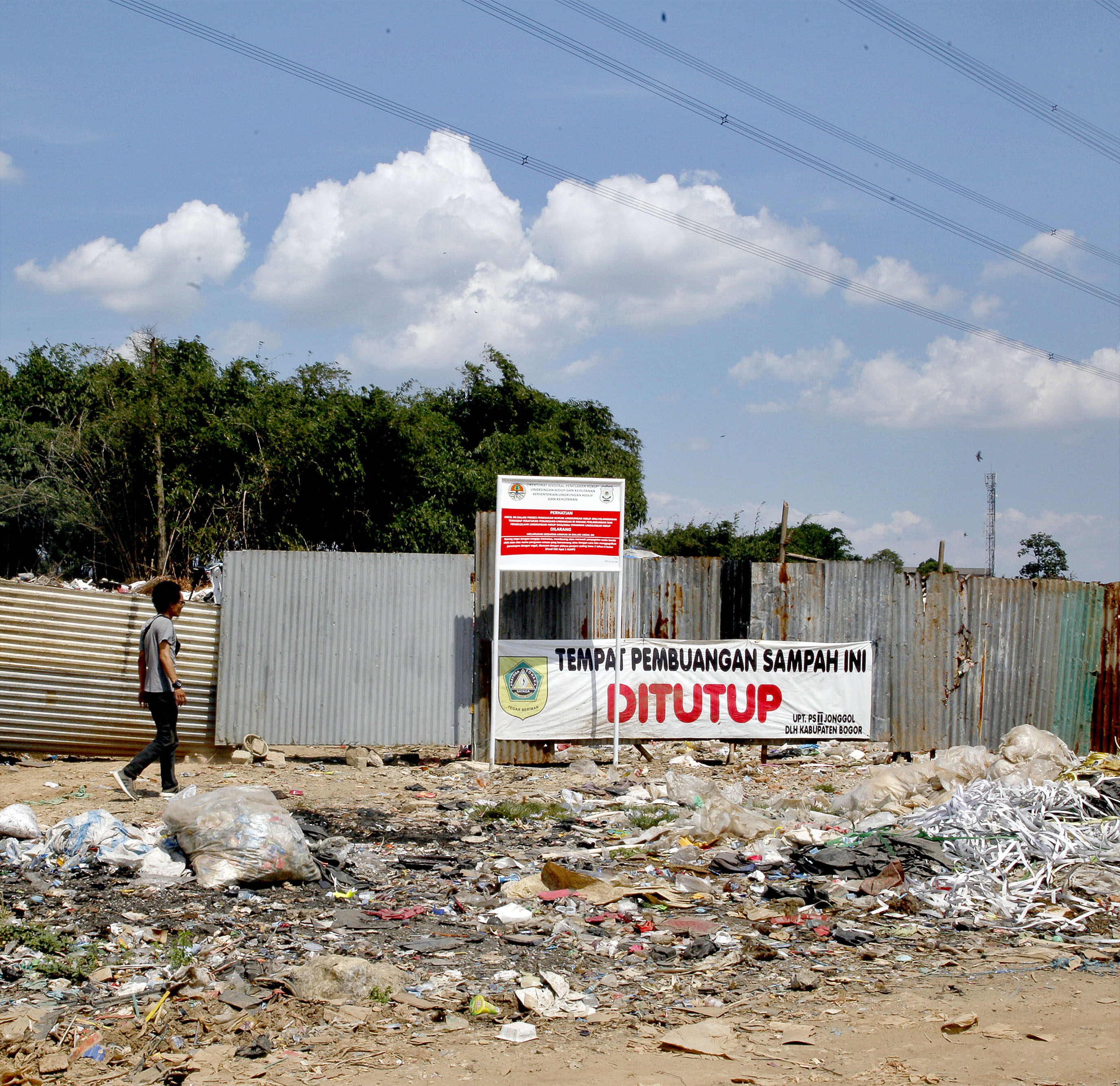 Warga melintas di samping tempat pembuangan sampah ilegal yang telah disegel di Limus Nunggal, Cileungsi, Bogor, Jawa Barat.