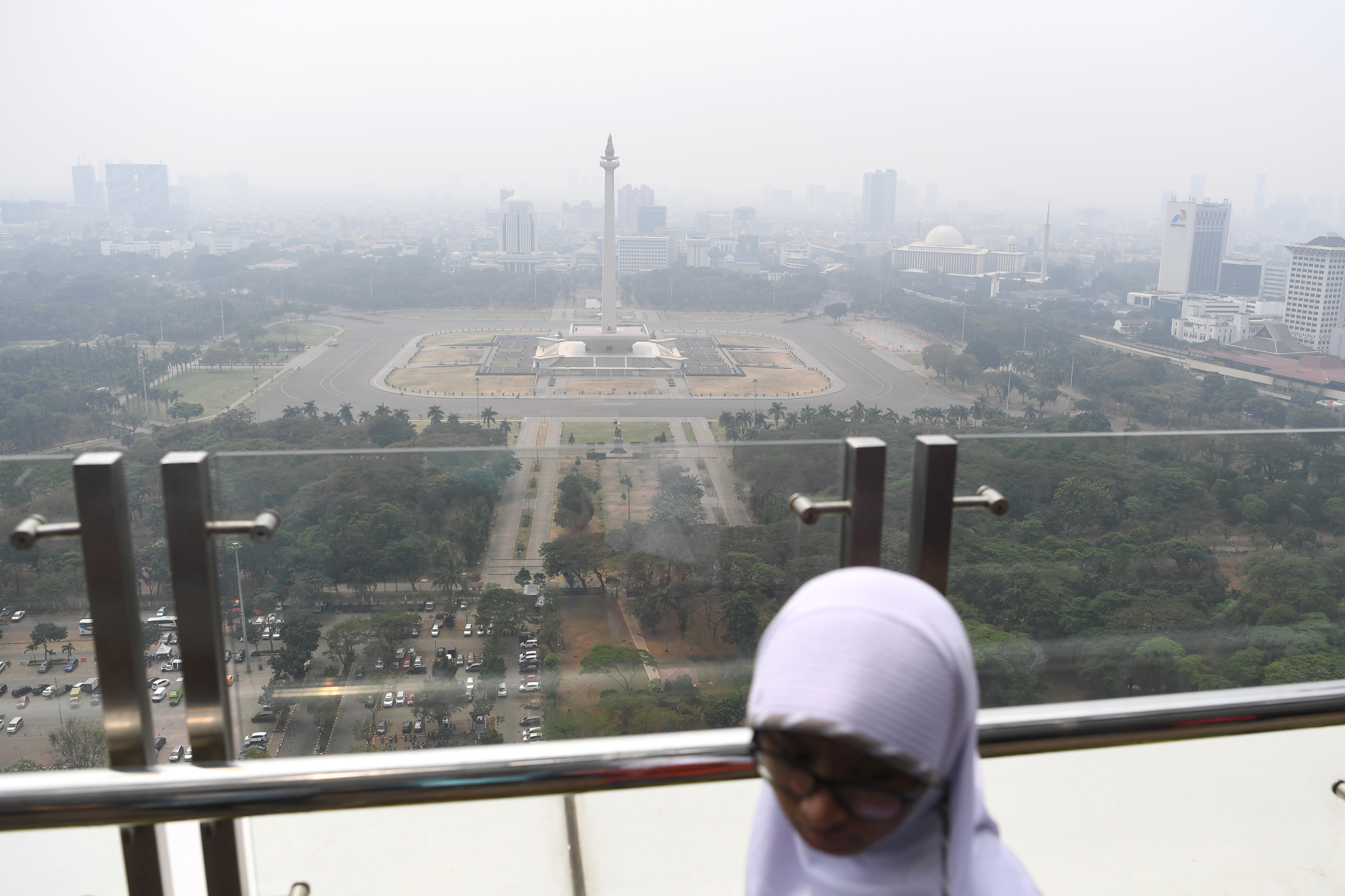Warga beraktivitas dengan latar belakang suasana gedung bertingkat yang diselimuti asap polusi di Jakarta.