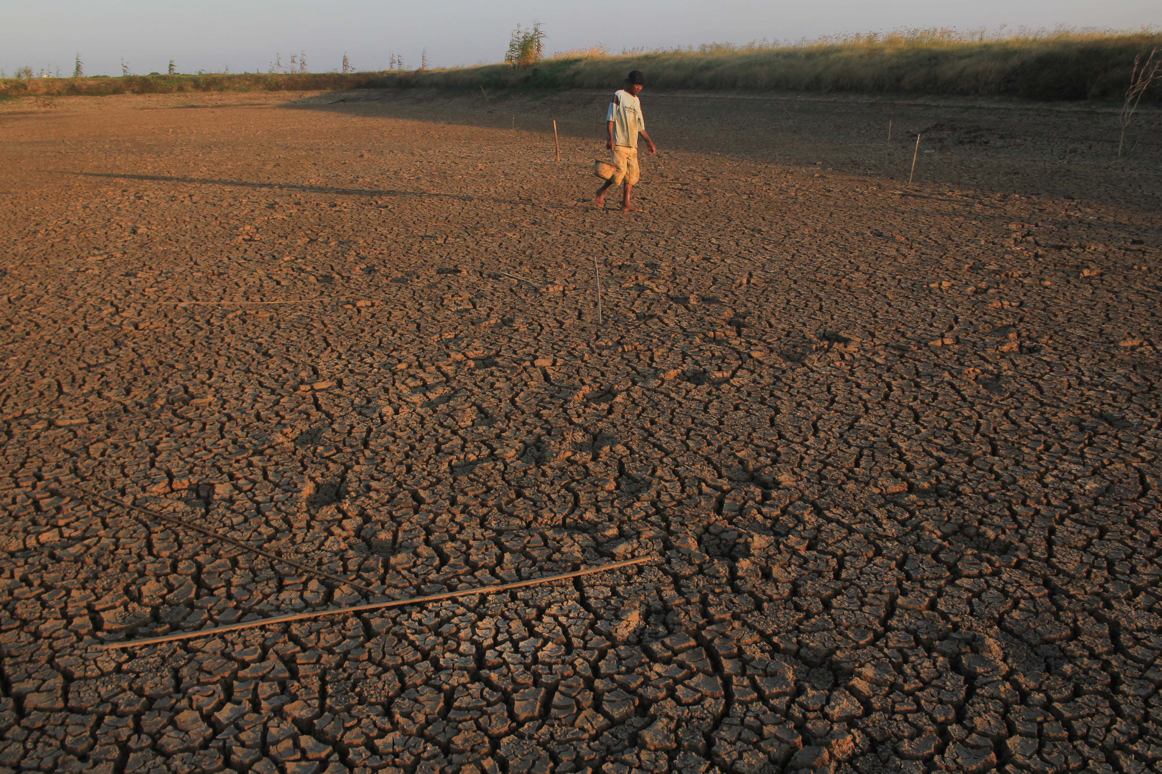 Petani berjalan di areal embung yang mengering di Balongan, Indramayu, Jawa Barat, Jumat (28/6/2019).