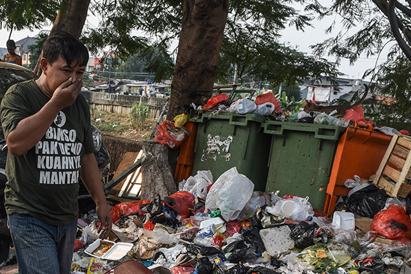Warga melintas di dekat tumpukan sampah rumah tangga di jalur Inspeksi Kanal Banjir Barat, Jakarta