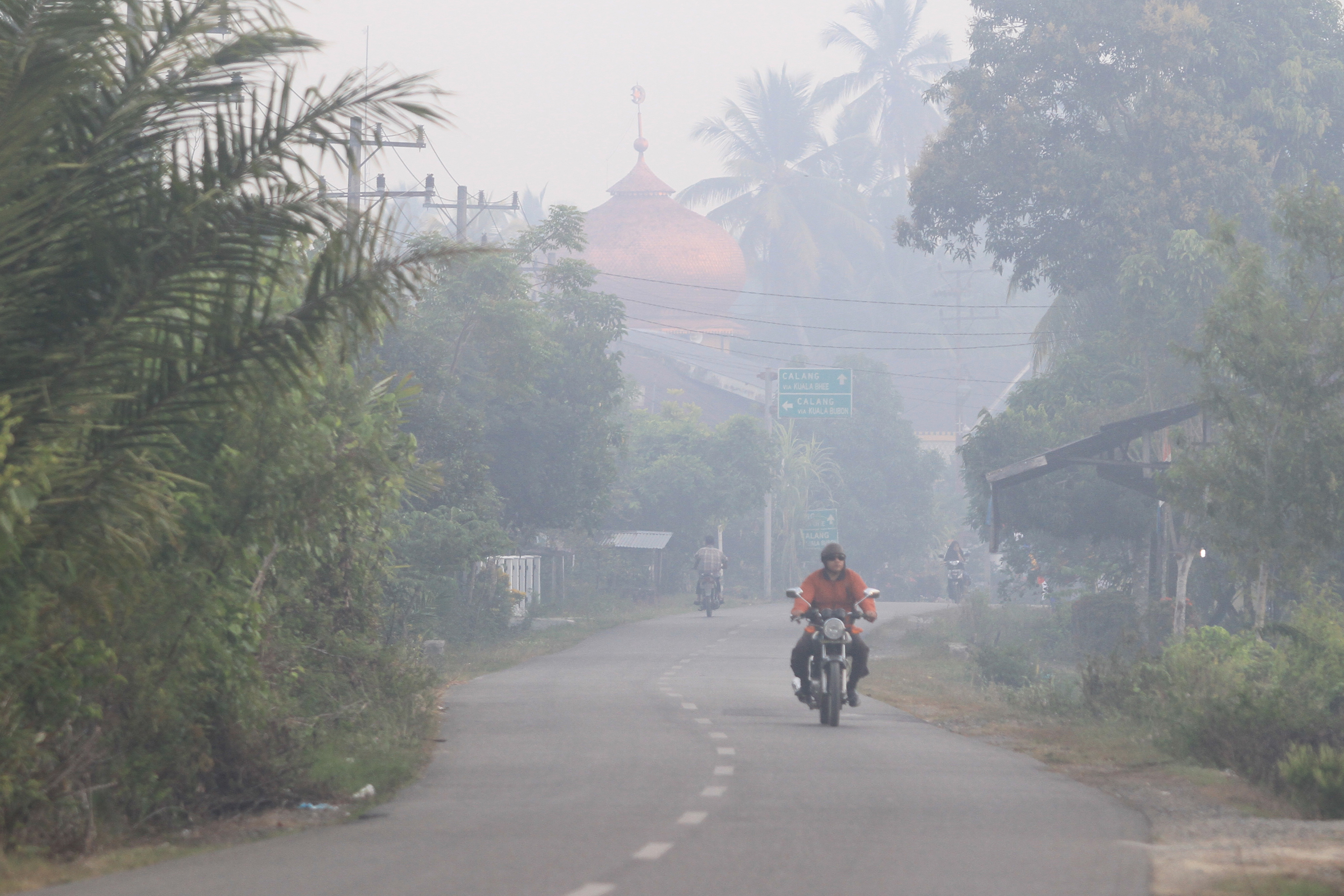 Pengendara sepeda motor melaju menembus kabut asap akibat Karhutla saat melintasi jalan Desa Pinem, Kecamatan Samatiga, Aceh Barat, Aceh.