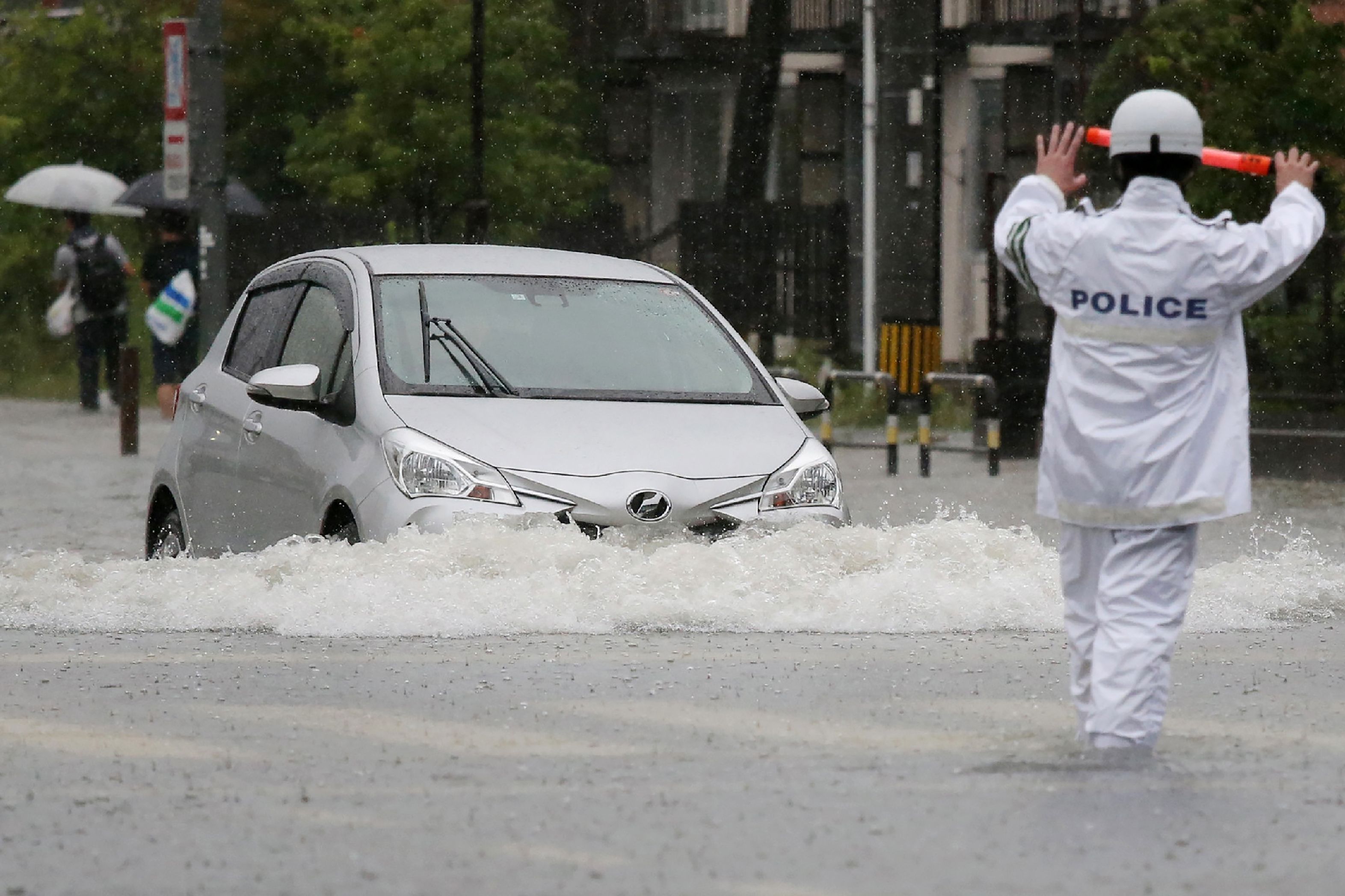 Seorang polisi menghentikan mobil yang tengah menembus banjir di Kota Saga, Jepang.