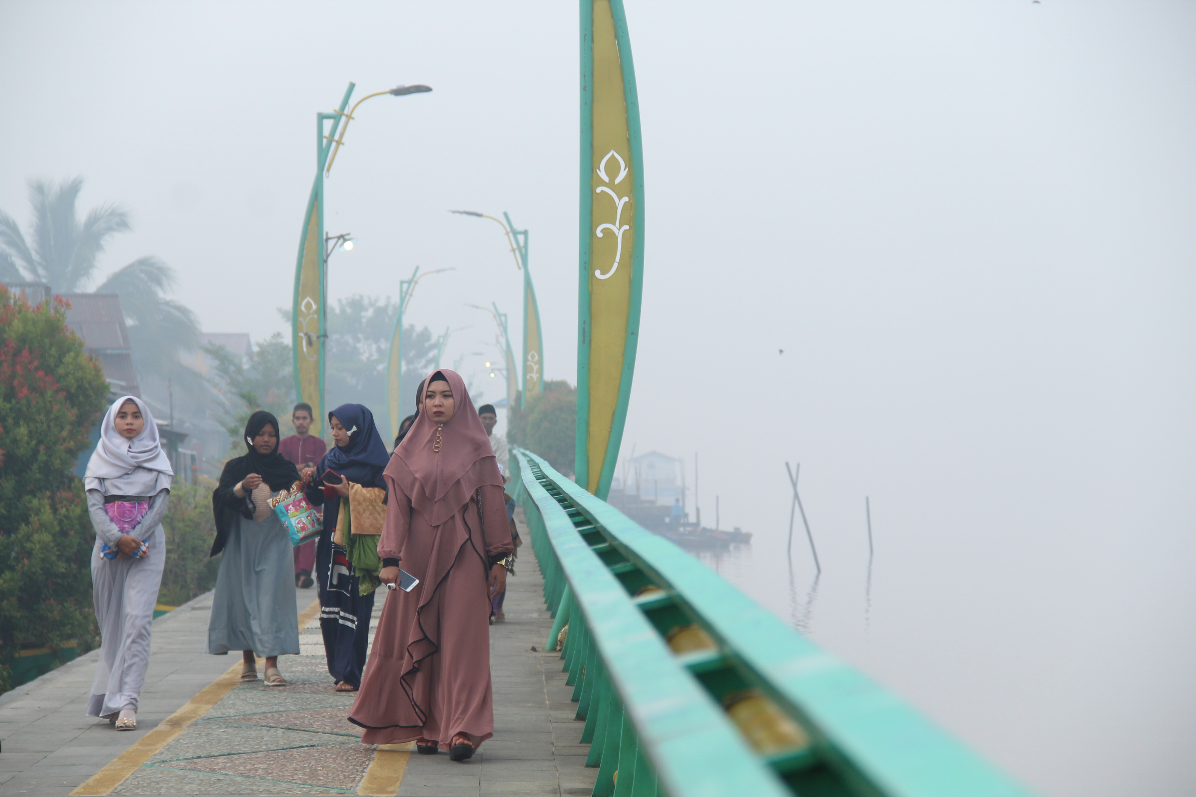 Warga berjalan di tepian Sungai Kapuas yang diselimuti kabut asap di Pontianak, Kalimantan Barat.