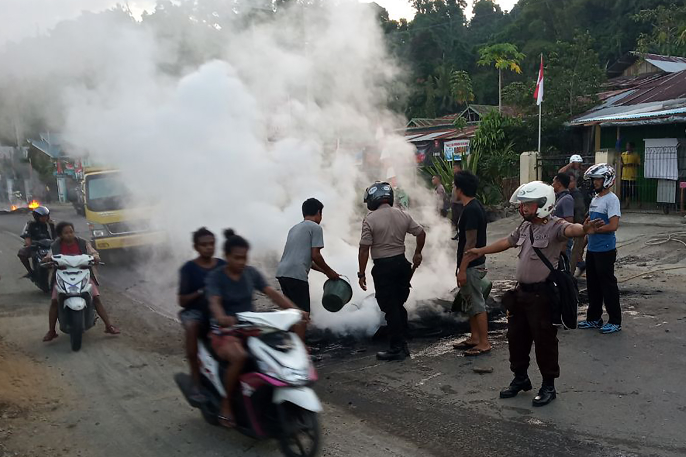 Petugas kepolisian bersama warga membersihkan ban yang dibakar seusai aksi di Jl.Essau Sesa Manokwari, Papua Barat.