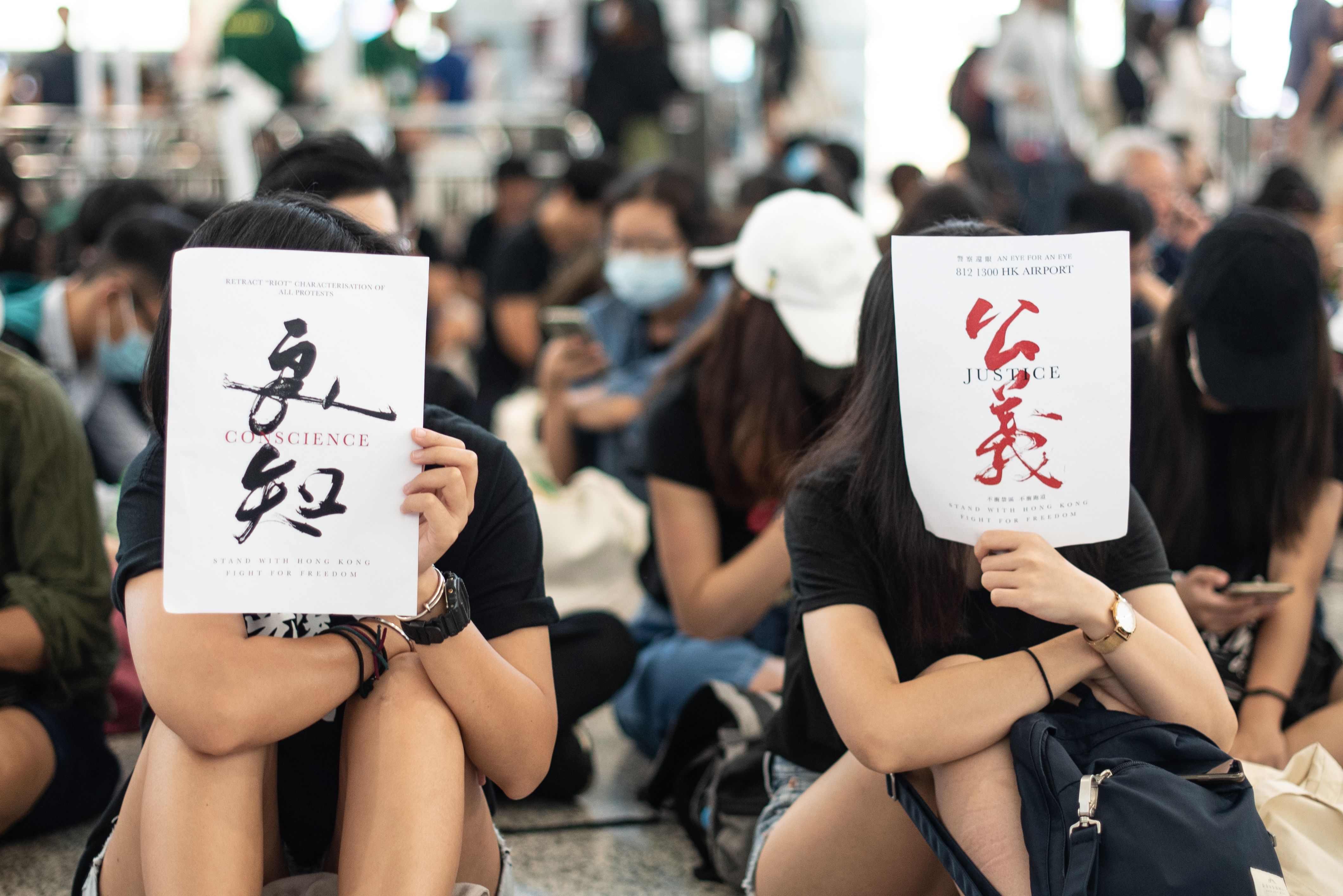 Dua demonstrans memegang lembaran kertas bertuliskan 'Hati Nurani' (kiri) dan 'Keadilan' (kanan) di Bandara Internasional Hong Kong.