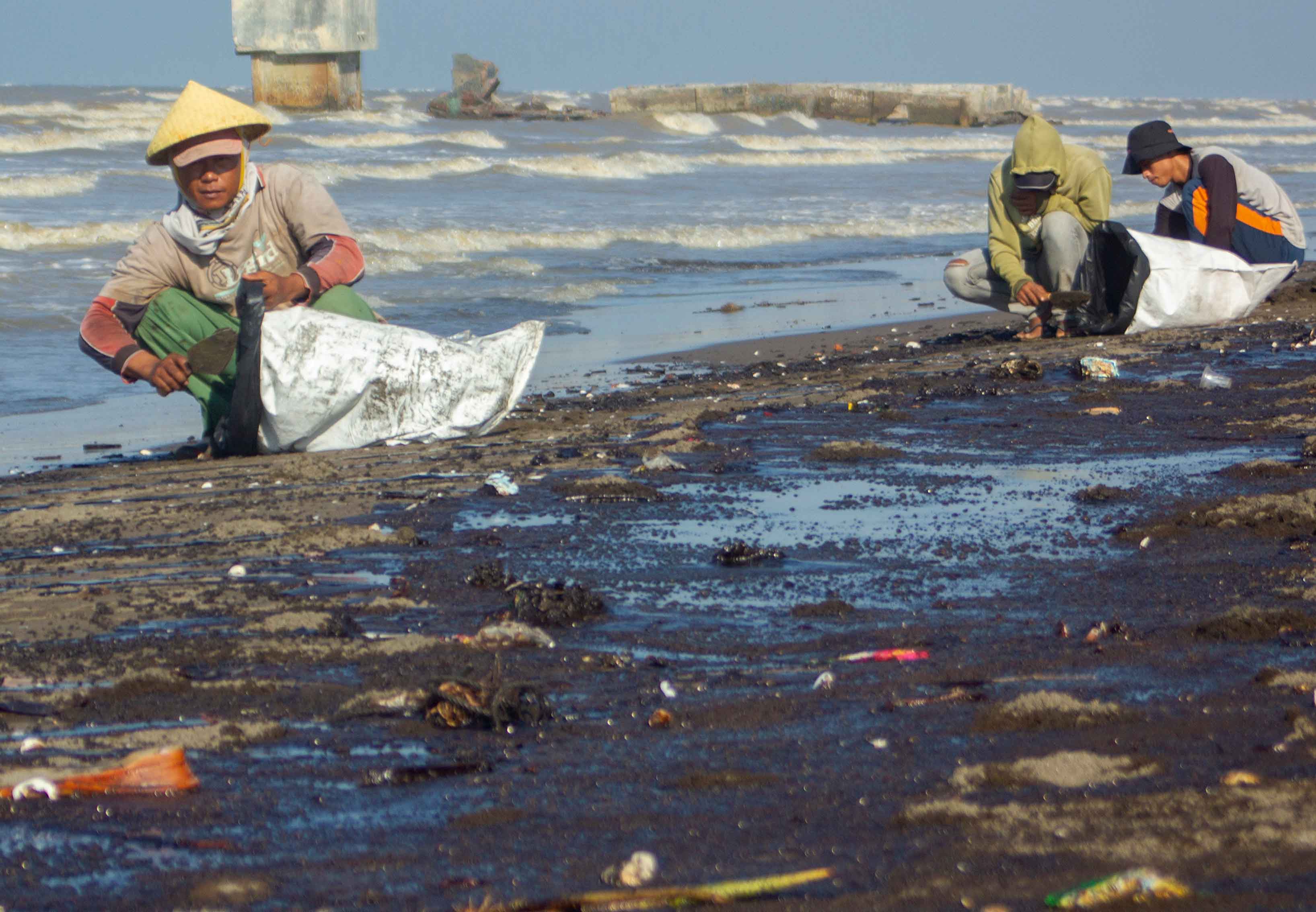 Warga mengumpulkan tumpahan minyak (Oil Spill) yang tercecer di Pesisir Pantai Cemarajaya, Karawang, Jawa Barat, Senin (22/7/2019). 