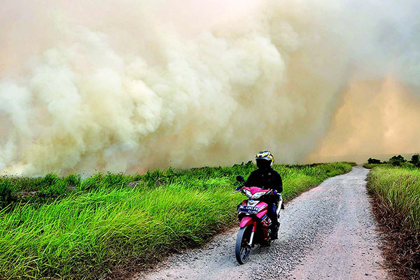 Warga melintasi lahan gambut yang terbakar di Desa Pulau Semambu, Indralaya Utara, Ogan Ilir, Sumatra Selatan, Senin (5/8).