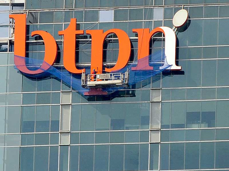 Pekerja menyelesaikan tugasnya di dekat lambang Bank Tabungan Pensiunan Negara (BTPN) di kawasan Kuningan