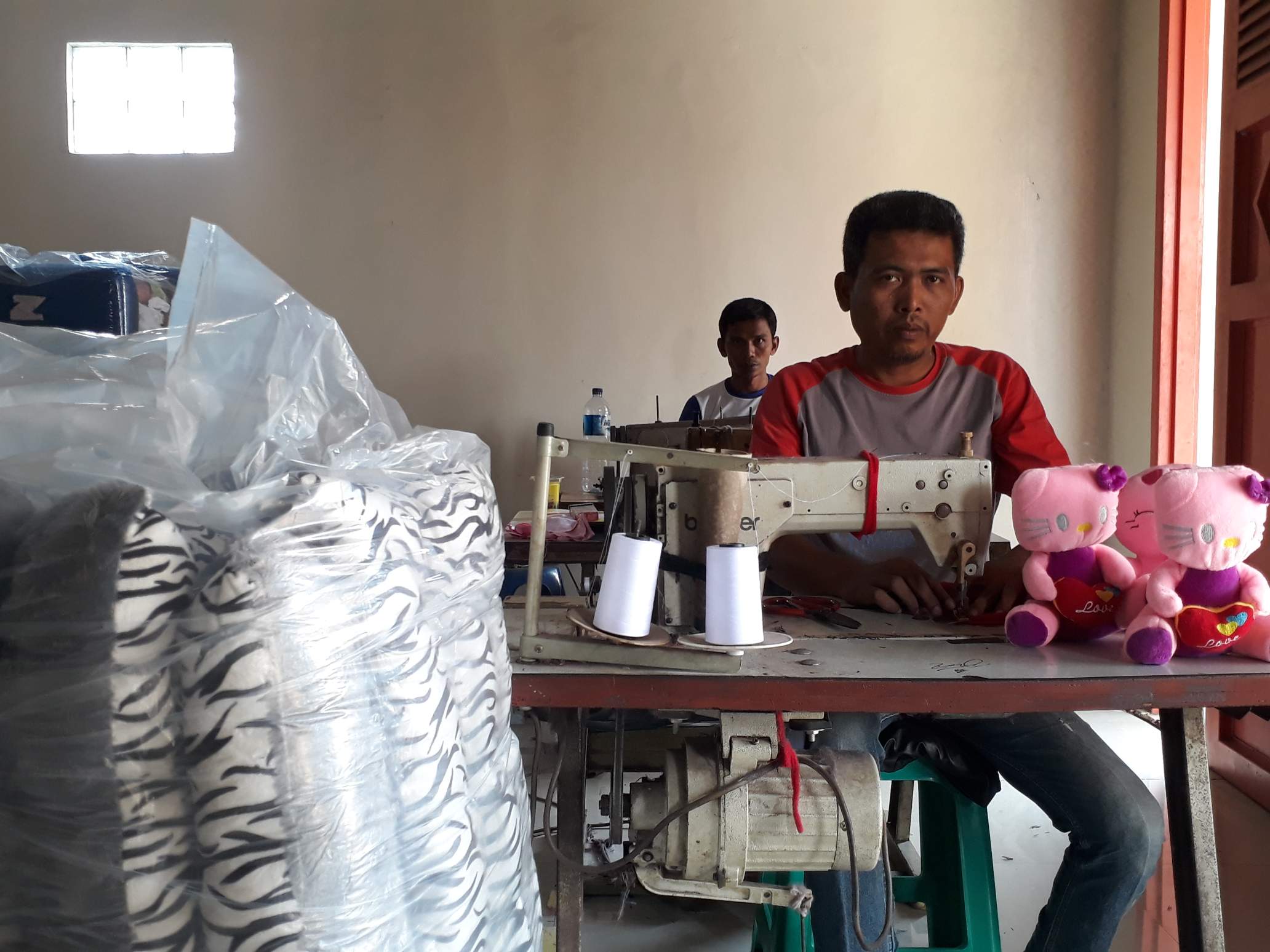 Agus Sopian tengah menjahit untuk membuat sebuah boneka kucing.