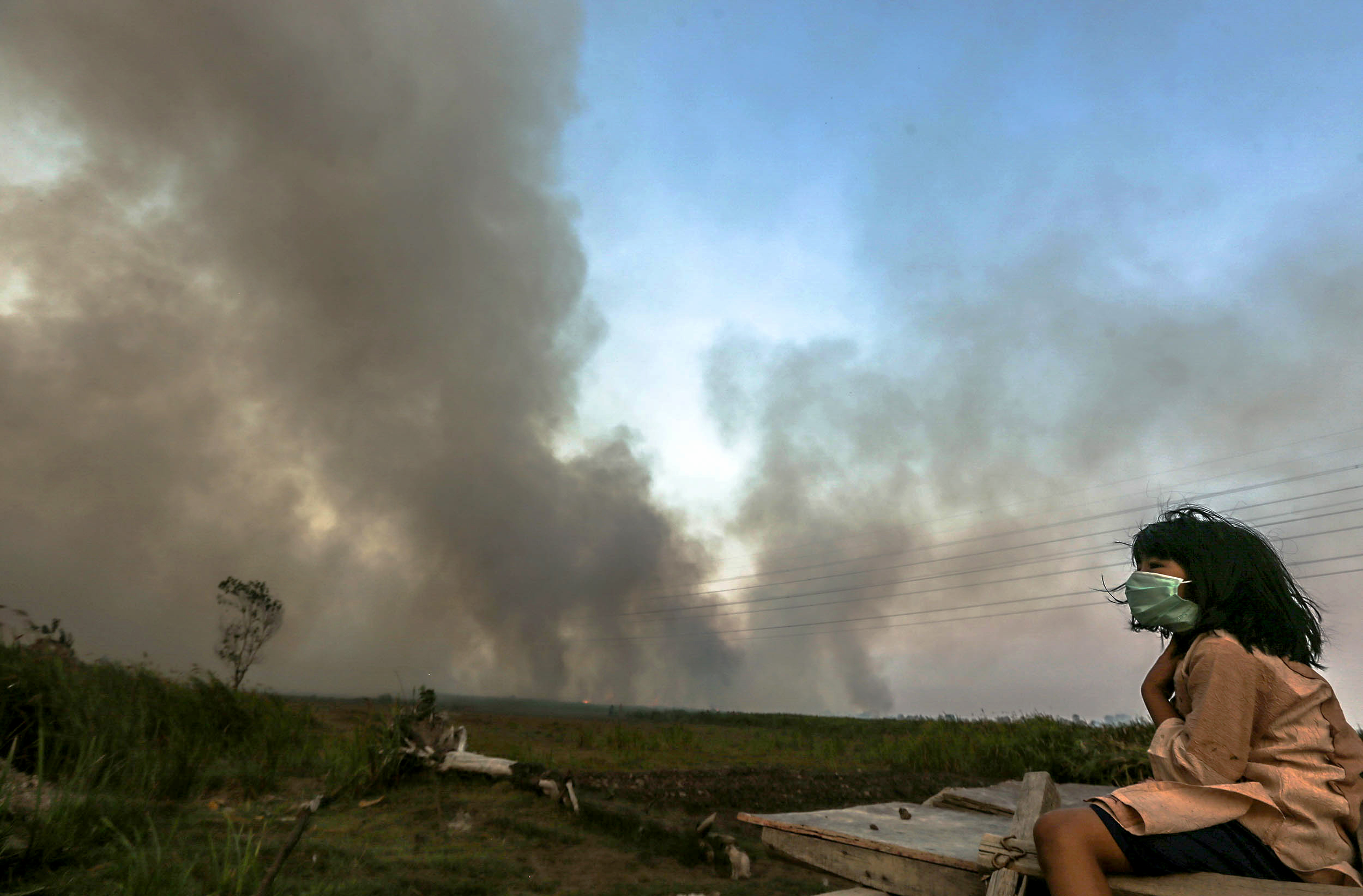 Seorang bocah duduk di depan rumahnya dengan mengunakan masker untuk melindungi dari asap kebakaran lahan.