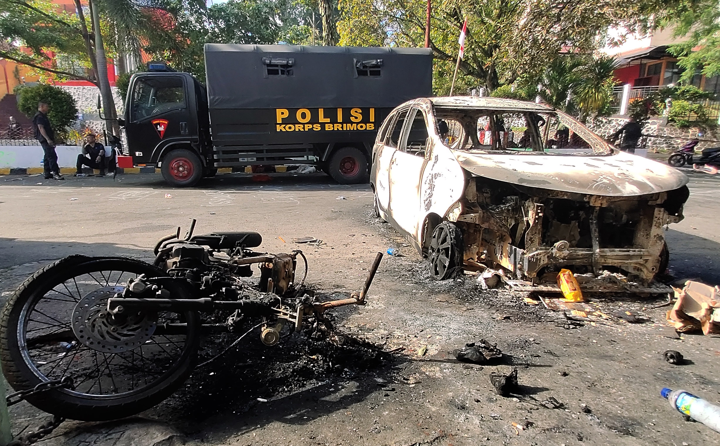 Dua personil Brimob berada di dekat kendaraan yang terbakar di Jayapura, Papua.