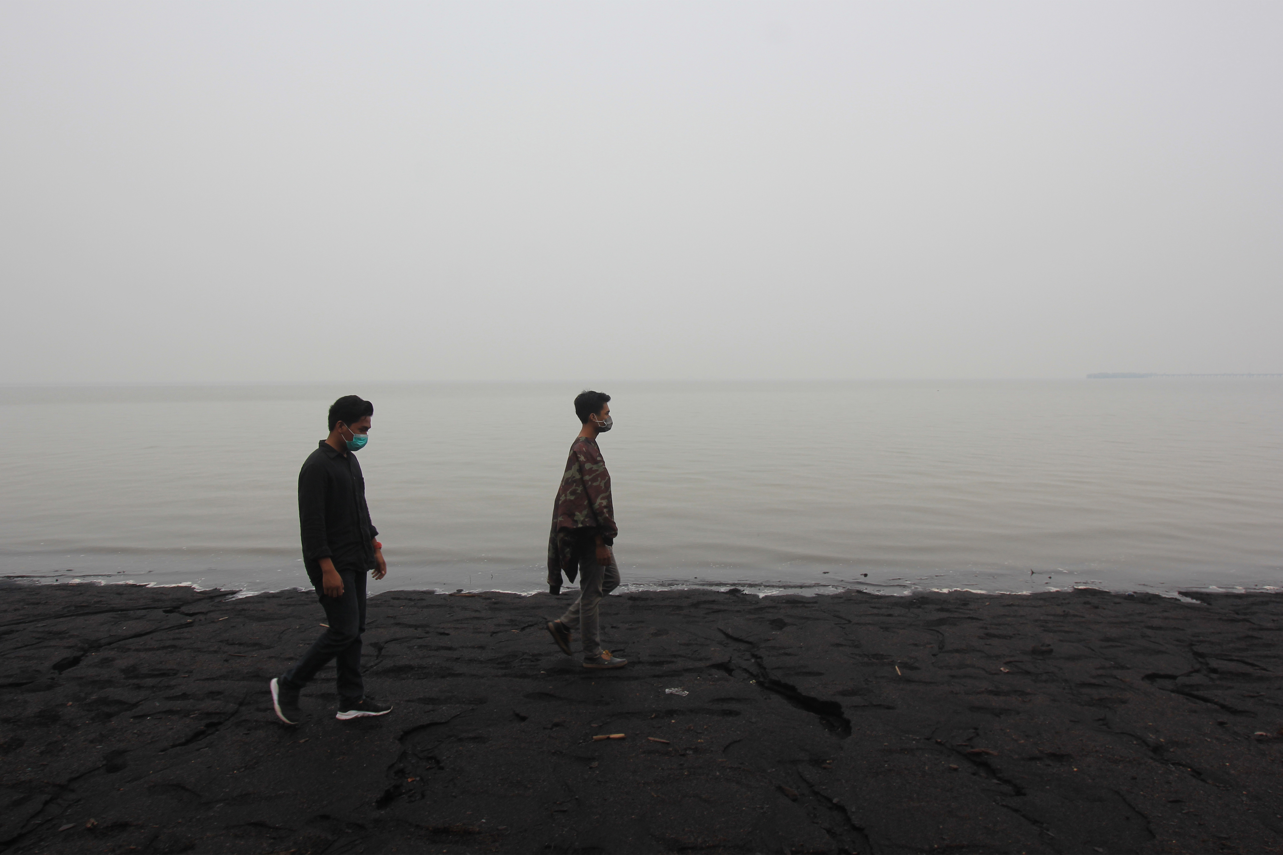  Wisatawan berjalan di Pantai Pulai Bungkuk Mundam yang diselimuti kabut asap kebakaran hutan di Dumai, Riau, Minggu (15/9)