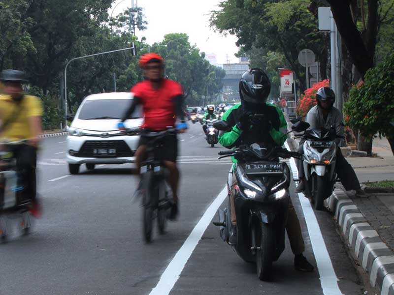 Pengendara sepeda melintas di luar jalur sepeda karena terhalang pengendara motor di Jalan Medan Merdeka Selatan, Jakarta Pusat.